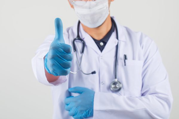 Smiling male doctor in white coat and mask making thumb up and looking happy . front view.